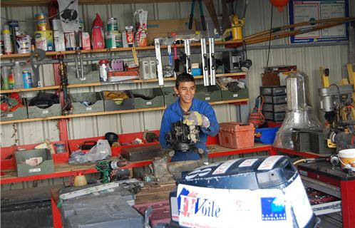 Un stagiaire passionné de mécanique est aux prises avec un moteur de hors-bord de l'école de voile du Yacht-club