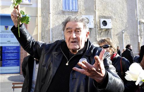 Armand Gatti, rose blanche tendue, en hommage aux jeunes résistants allemands fusillés en 1943. Droits réservés.